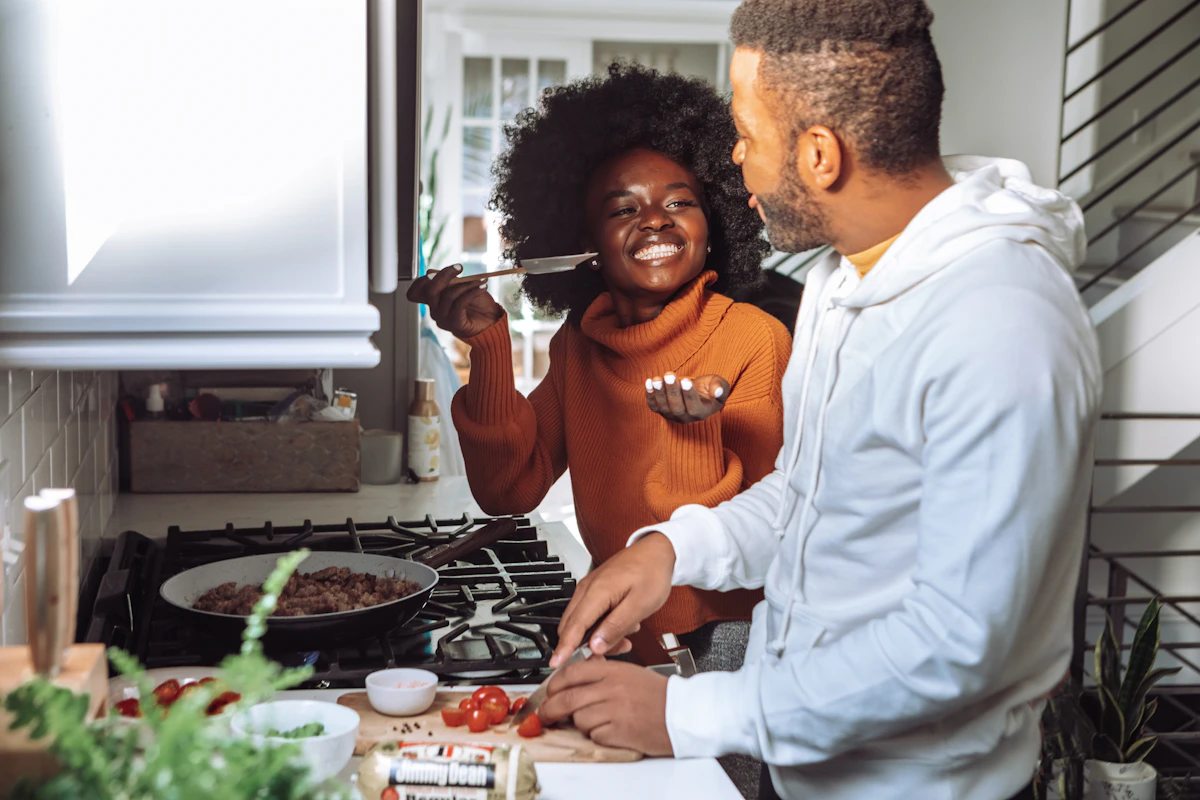 A couple laughing together while cooking a meal at the stove
