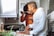A couple is in a kitchen, engaged in cooking together. One person is tasting food from a spoon offered by the other, creating a joyful and interactive atmosphere.