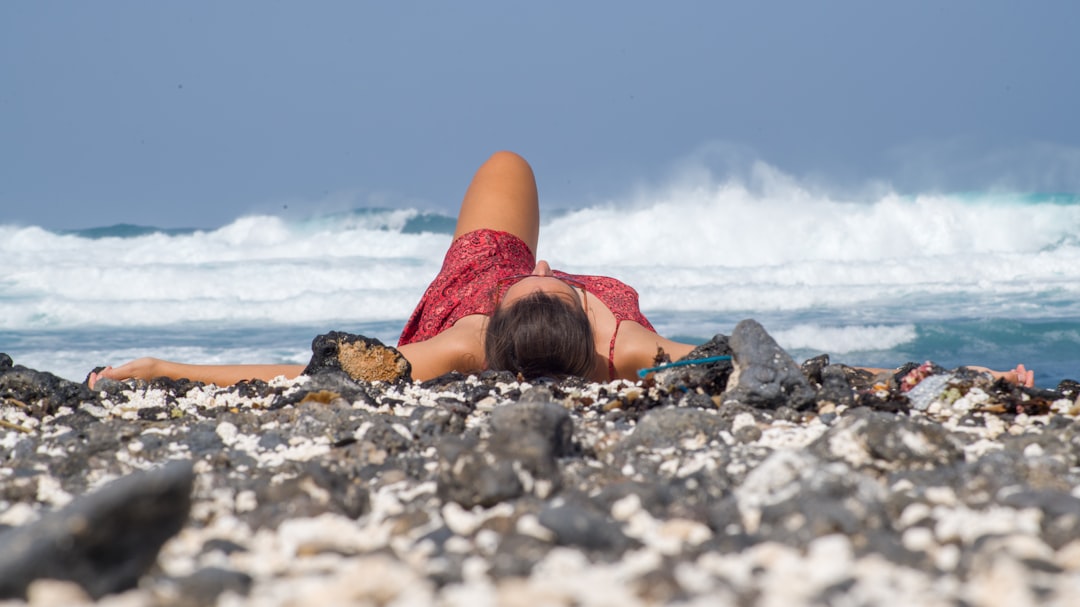 woman in pink tank top lying on rocky shore during daytime
