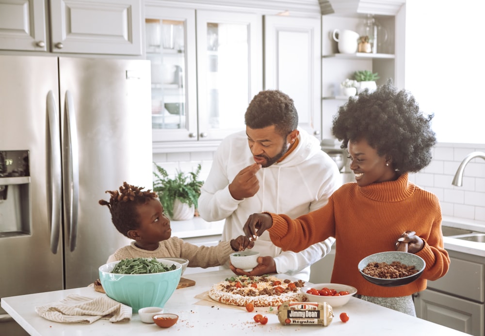 man in orange sweater sitting beside woman in white long sleeve shirt eating pizza