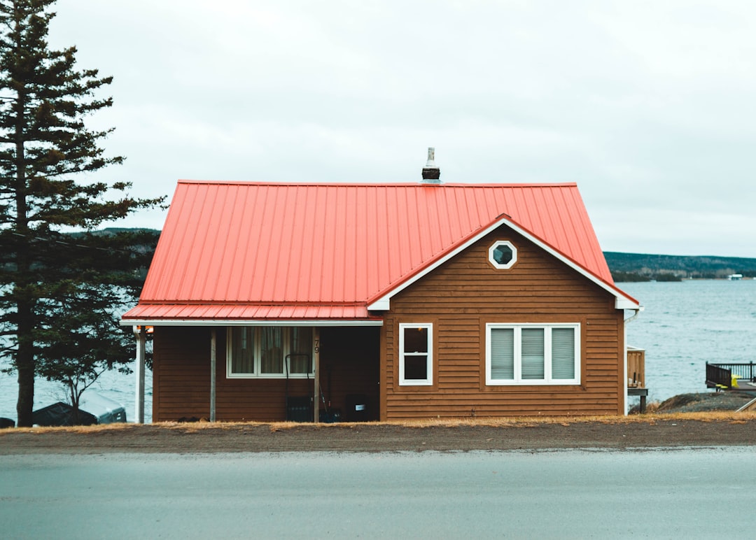 red and white wooden house near green trees under white clouds during daytime,