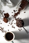 coffee beans on white ceramic mug beside stainless steel spoon