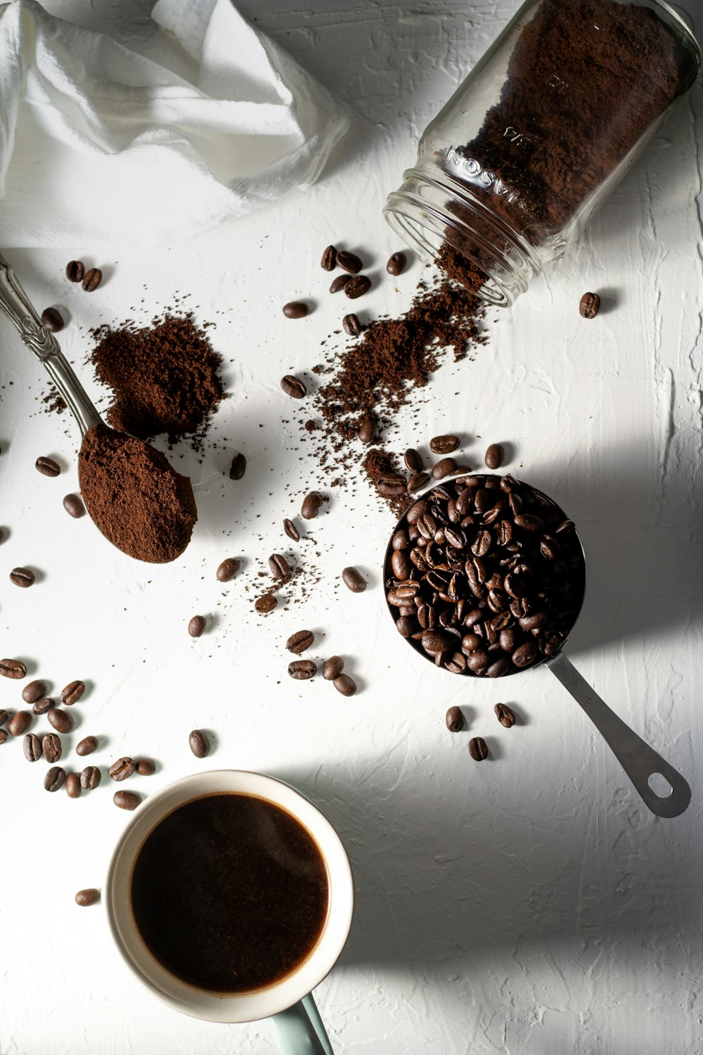 grains de café sur tasse en céramique blanche à côté de la cuillère en acier inoxydable