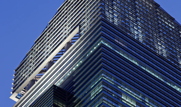 A modern skyscraper with sleek glass panels and a prominent logo at the top. The architecture features a mix of vertical and horizontal lines, creating a striking geometric design against the evening sky.