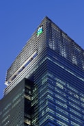 A modern skyscraper with sleek glass panels and a prominent logo at the top. The architecture features a mix of vertical and horizontal lines, creating a striking geometric design against the evening sky.
