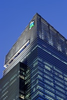 A modern skyscraper with sleek glass panels and a prominent logo at the top. The architecture features a mix of vertical and horizontal lines, creating a striking geometric design against the evening sky.