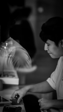 A grayscale image depicts a person focusing intently while holding a card or material, with blurred reflections and a soft, dim background.