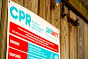 A sign detailing cardiopulmonary resuscitation (CPR) instructions, positioned against a wooden wall. The text includes warnings and response tips and highlights the importance of supervision around pools.