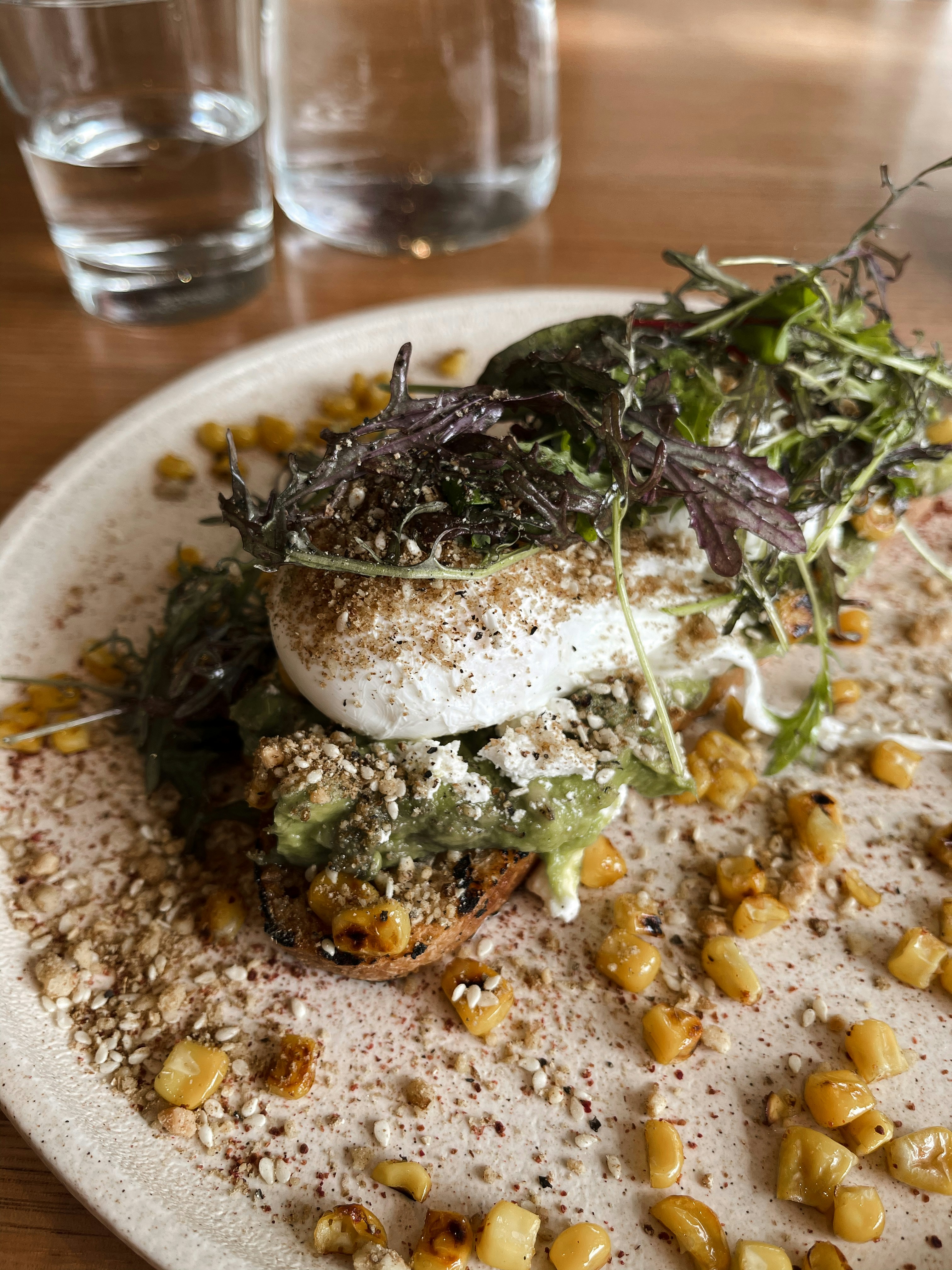 A poached egg under micro herbs on a plate scattered with corn kernels
