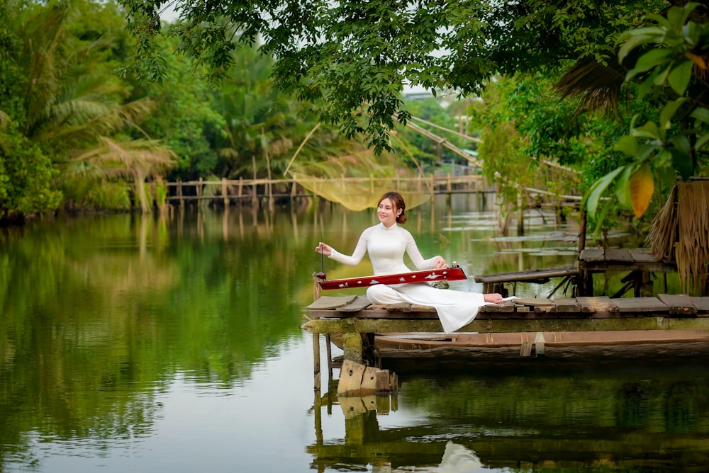 woman in white dress sitting on brown wooden bench near body of water during daytime