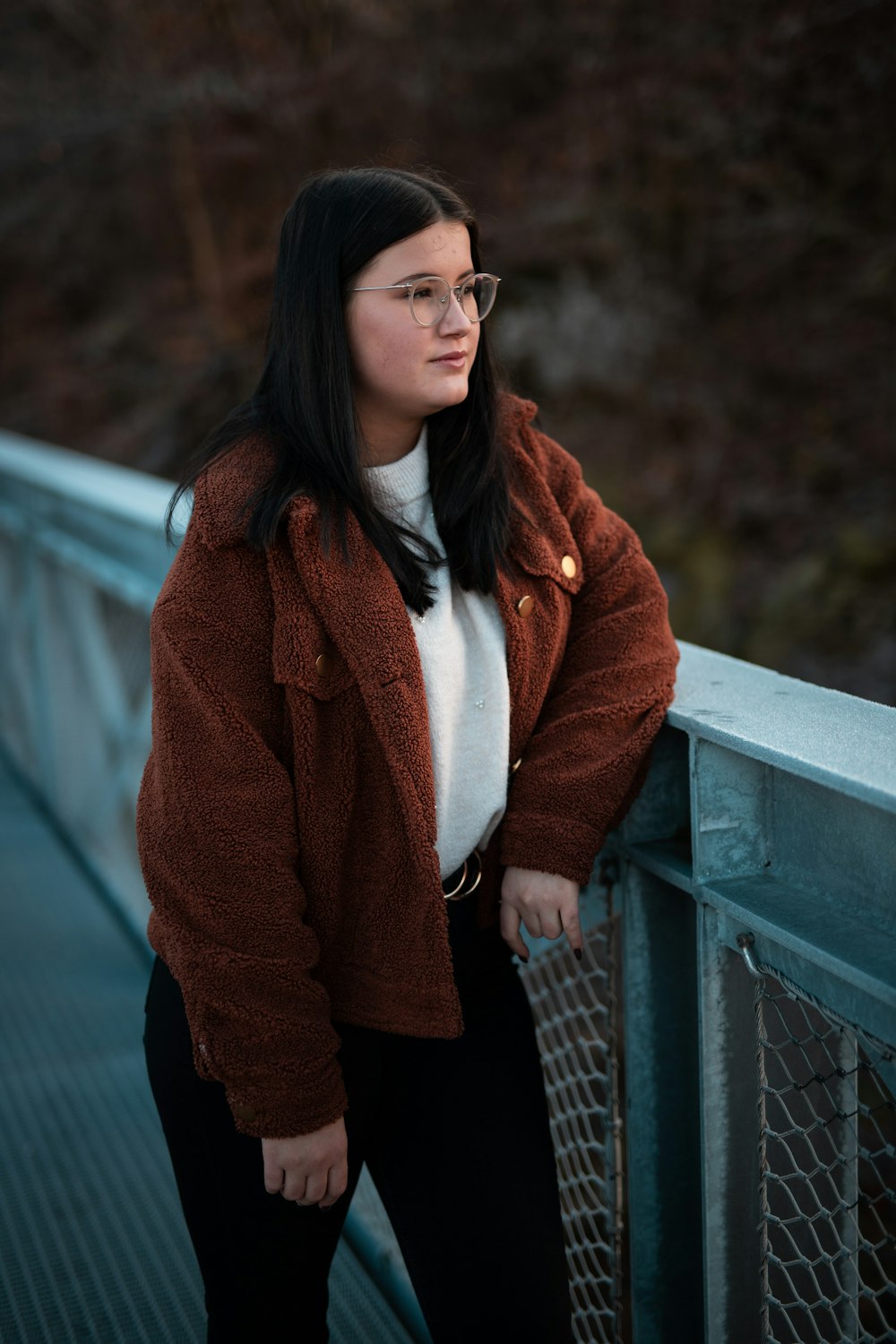 a woman leaning against a fence with her hands on her hips