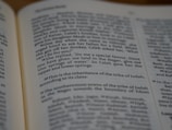 A close-up view of an open book showing text from a religious scripture with bold verse numbers. The page is slightly angled, focusing on a specific passage.