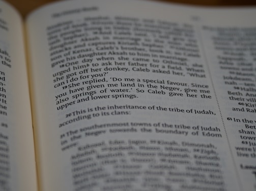 A close-up view of an open book showing text from a religious scripture with bold verse numbers. The page is slightly angled, focusing on a specific passage.