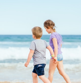 boy in white t-shirt and blue shorts standing on seashore during daytime