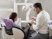 Dentist in white smock sitting and showing a female patient in a dental chair about treatment.