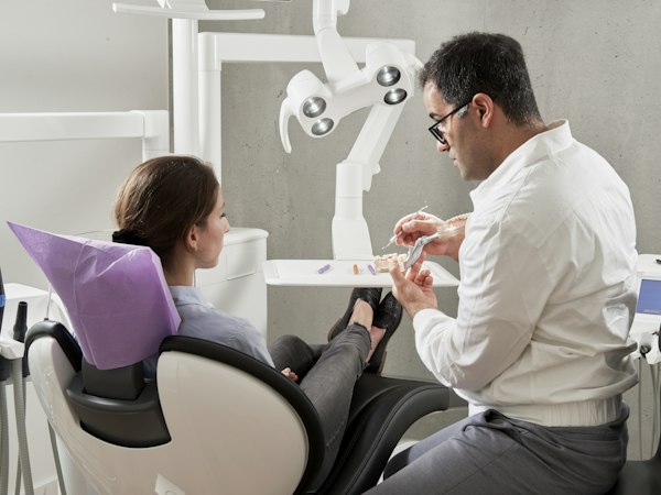 Odontólogo enseñando una maqueta dental a una paciente sentada en el sillón