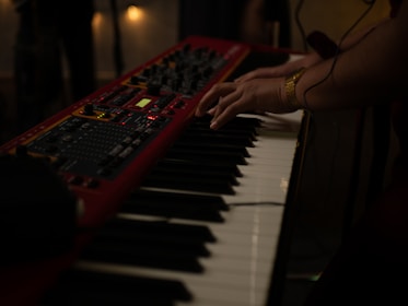 Close-up of vintage synthesizer keys glowing under dim red lighting, with the male keyboardist’s hands poised to play.