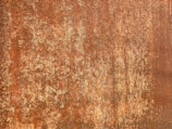 A textured surface with a rusty appearance, featuring a mix of browns and reddish-orange hues with a rough, corroded texture.