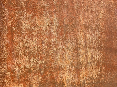 A textured surface with a rusty appearance, featuring a mix of browns and reddish-orange hues with a rough, corroded texture.