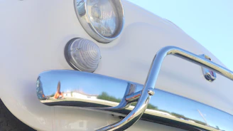 Close-up of a vintage Beetle's round headlight and chrome bumper gleaming under sunlight