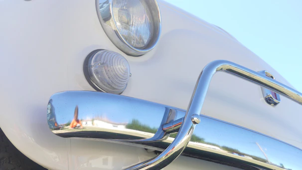 Close-up of a vintage Beetle's round headlight and chrome bumper gleaming under sunlight