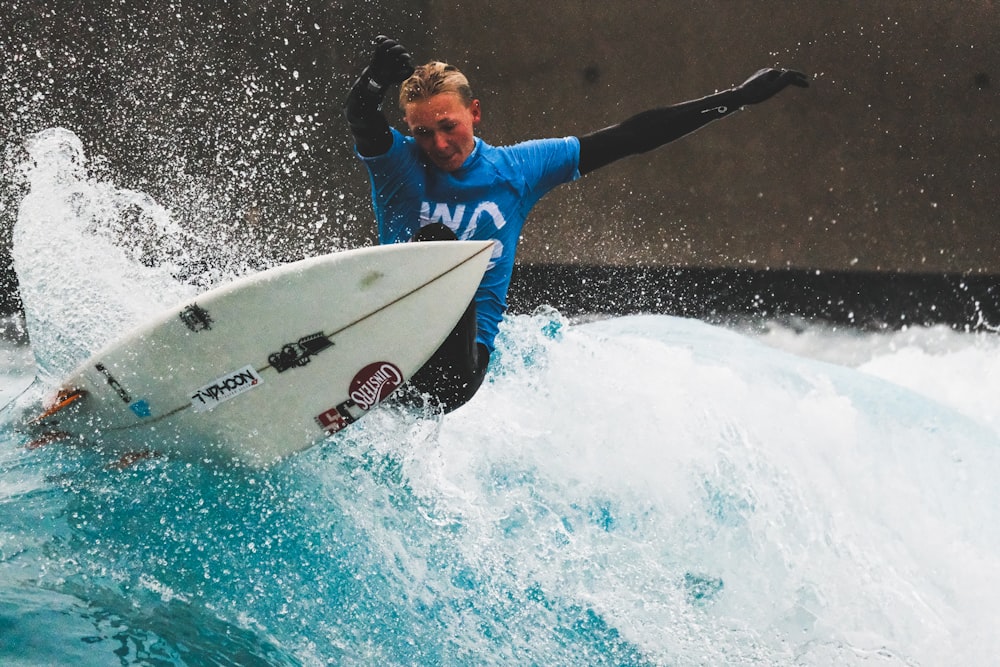 man in blue and white wet suit holding white surfboard