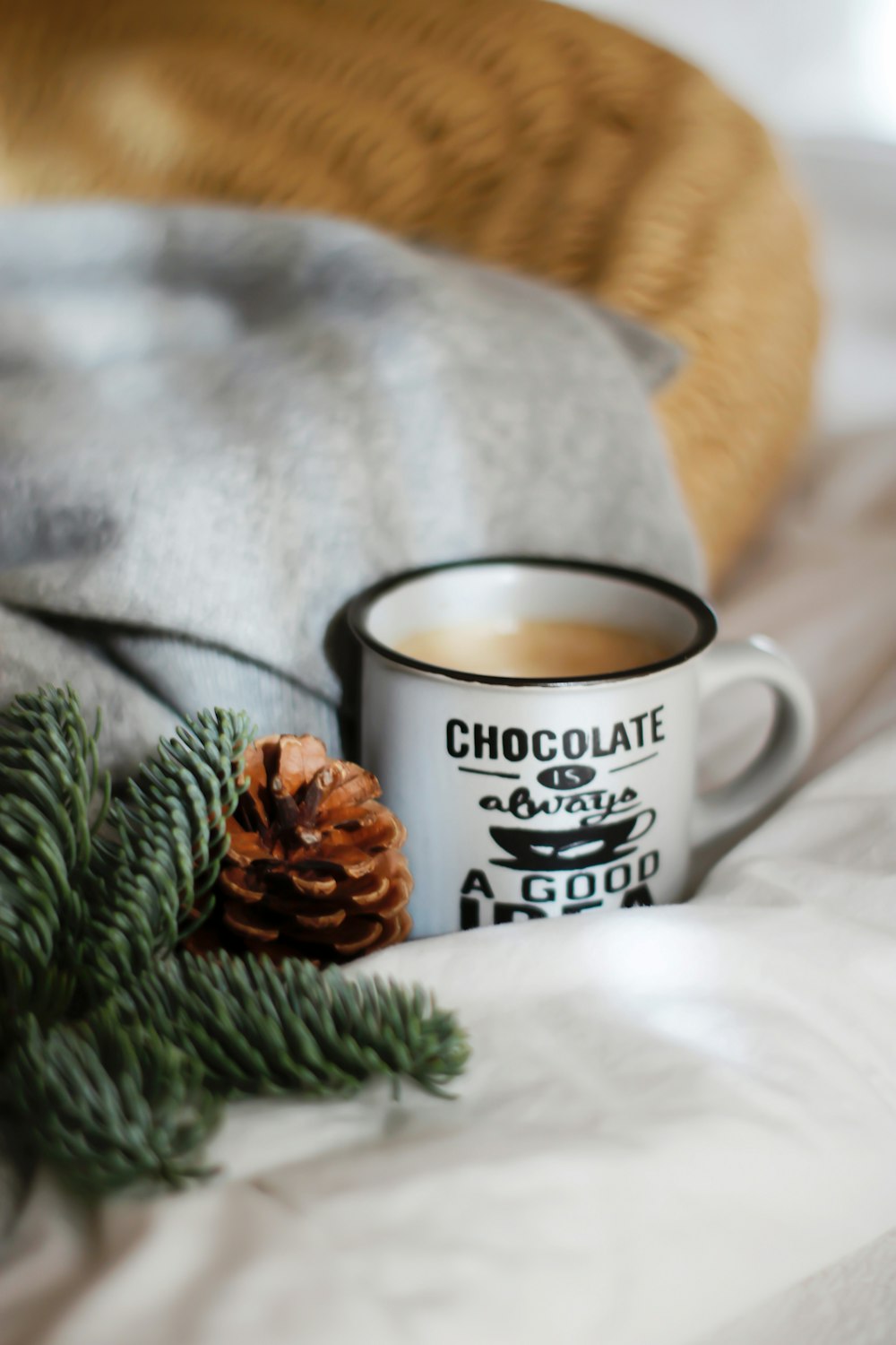 white and black ceramic mug beside pine cones on white textile