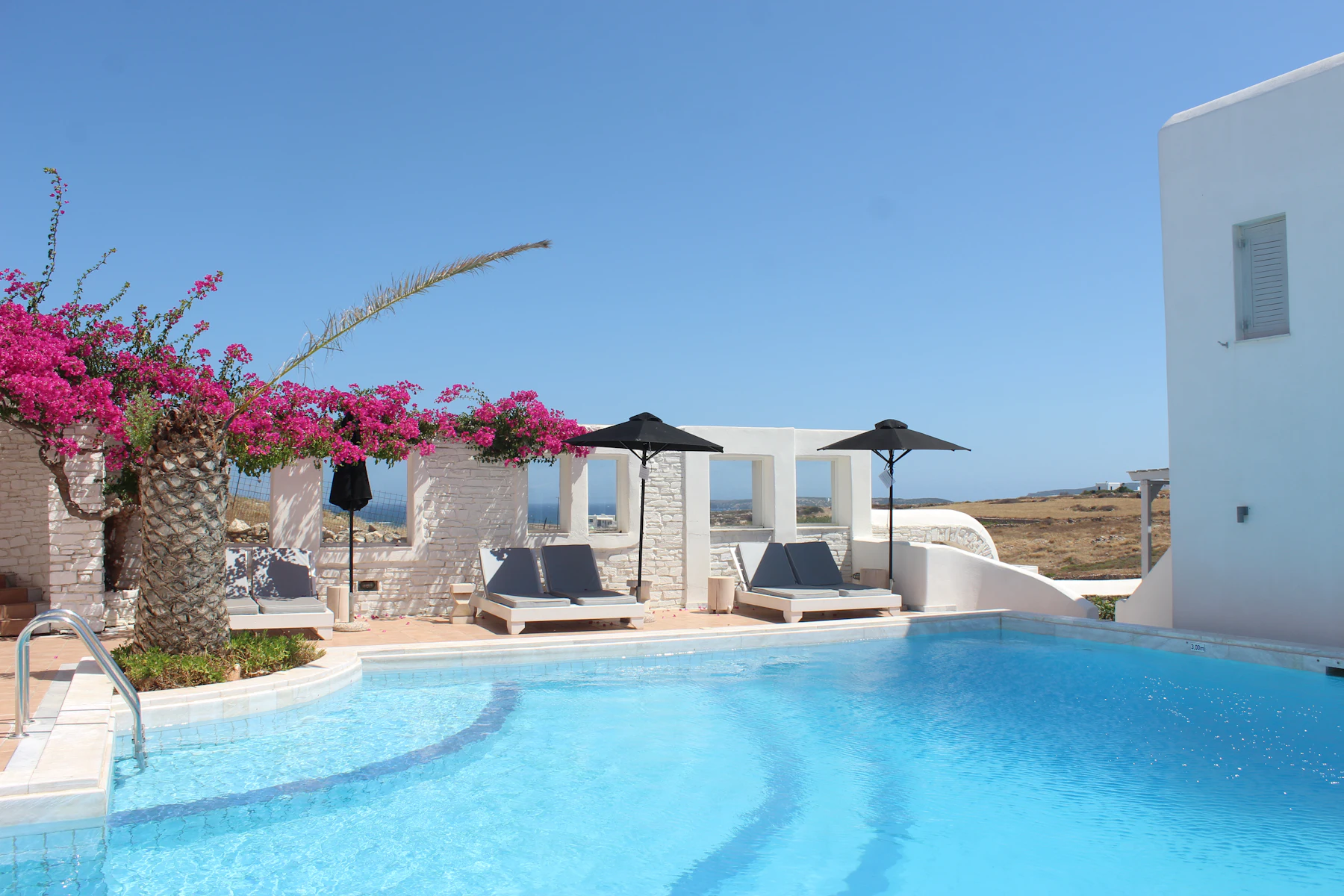 A whitewashed villa with shaded loungers beside a pool, the sea beyond