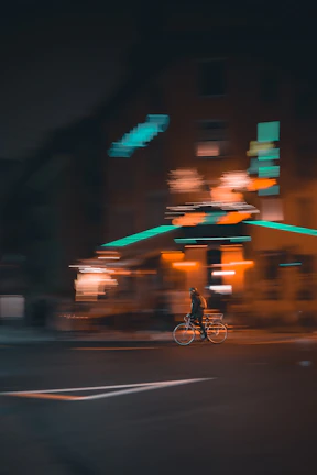 Dynamic shot of a young rider performing a wheelie through city streets guarded by glowing orange neon streetlights.