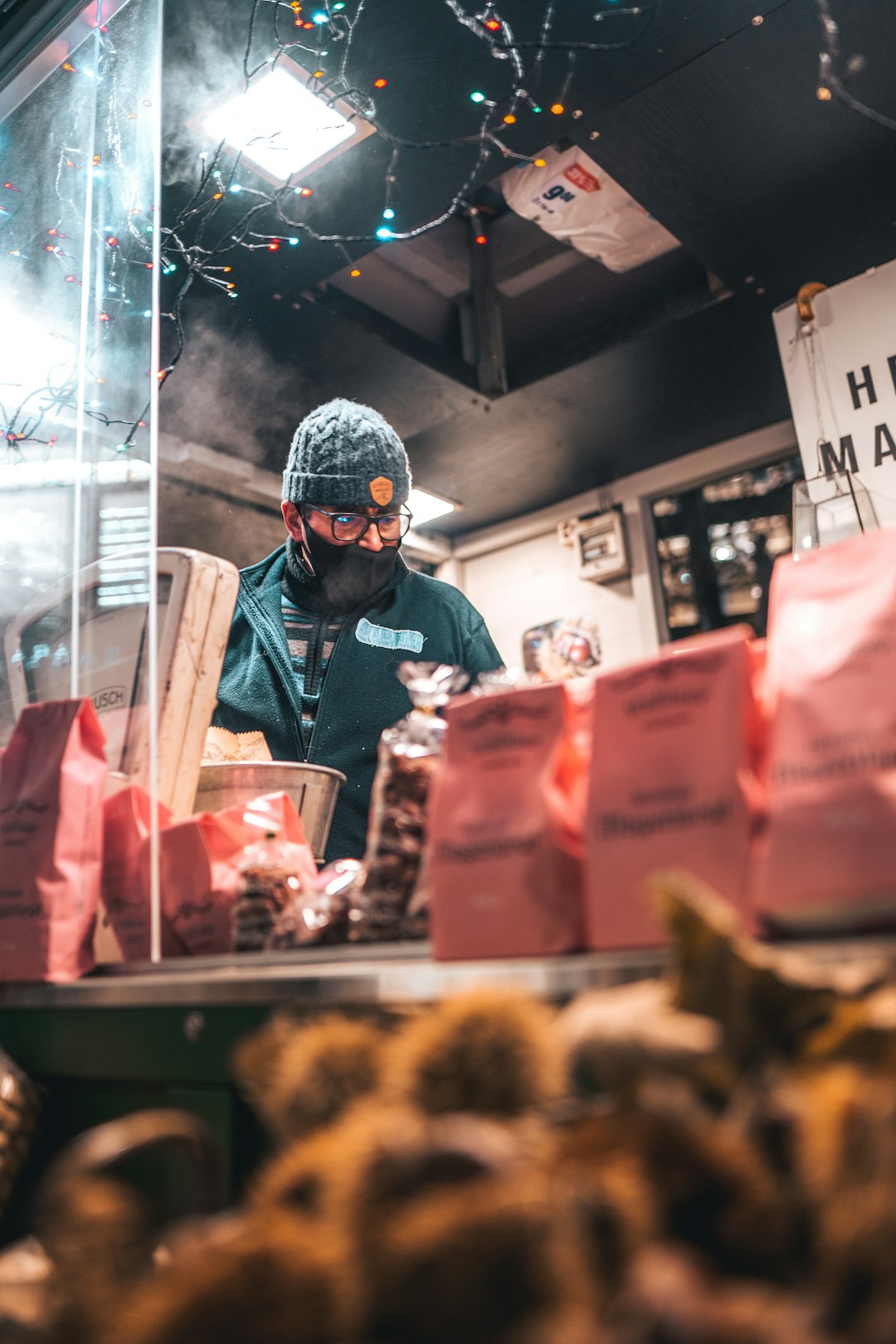 man in black jacket and black knit cap standing in front of food stall