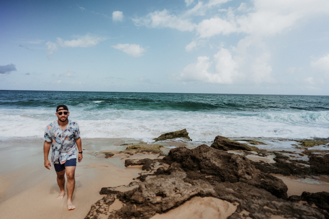 woman in blue and white floral shirt standing on brown rock near sea during daytime