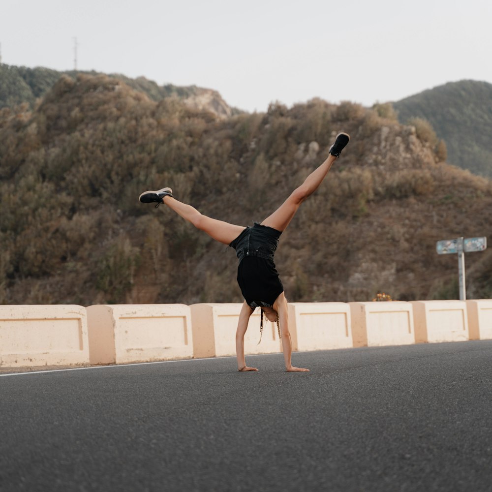 woman in black tank top and black shorts jumping on gray asphalt road during daytime