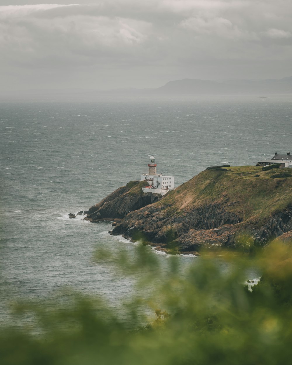 white lighthouse on green grass covered hill by the sea under white cloudy sky during daytime