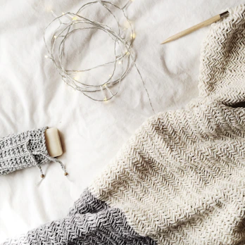 A plush, hand-knit blanket folded neatly on a soft grey sofa.