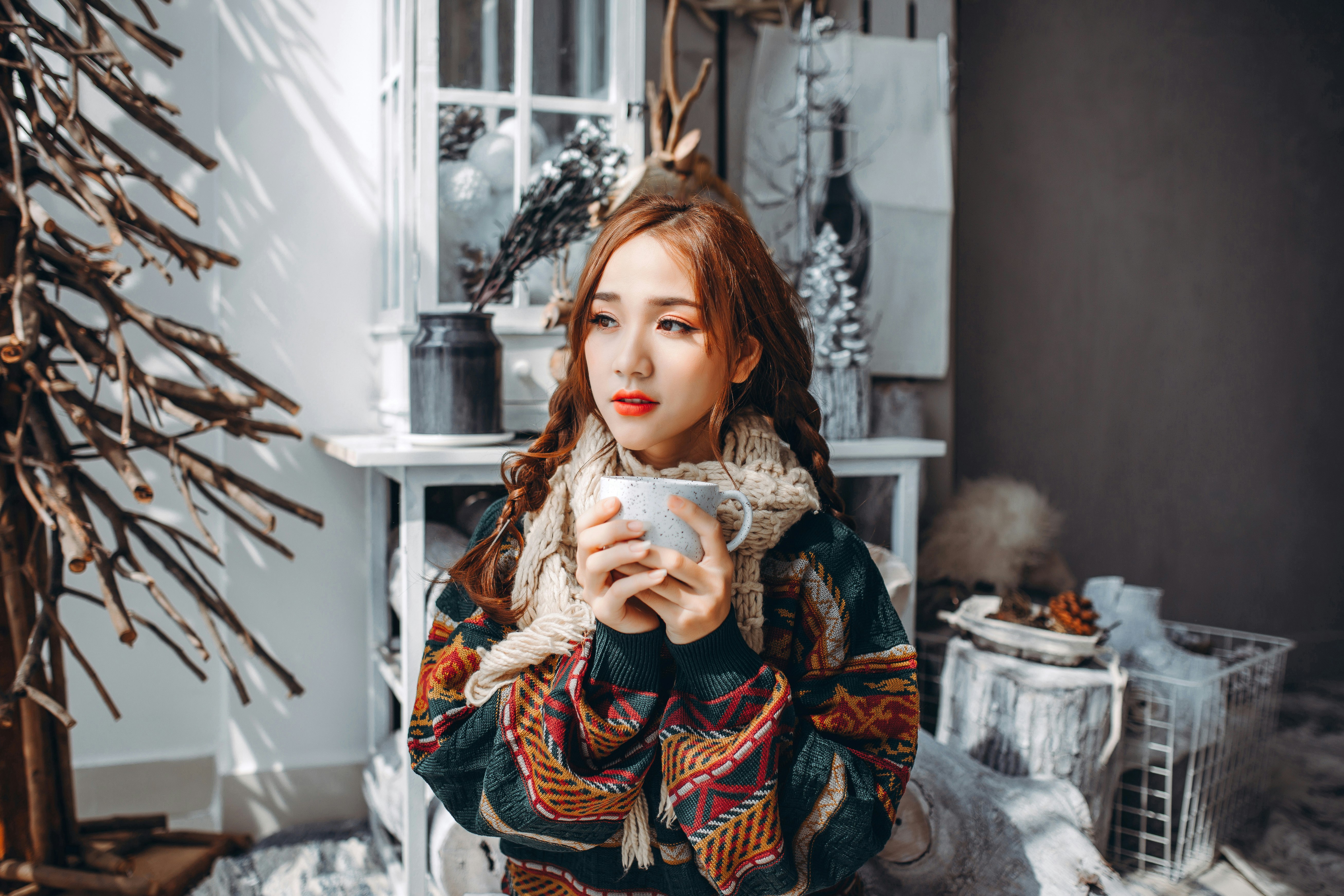 woman in brown and white tribal coat holding white ceramic mug