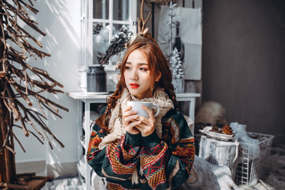 Femme en manteau tribal marron et blanc tenant une tasse en céramique blanche