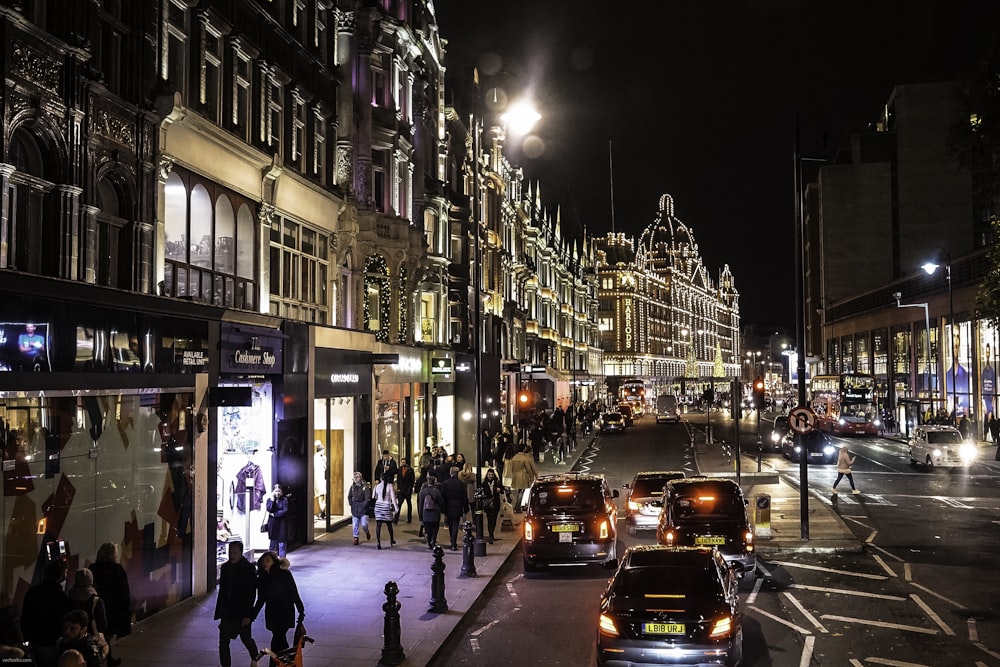 people walking on sidewalk near cars and buildings during night time