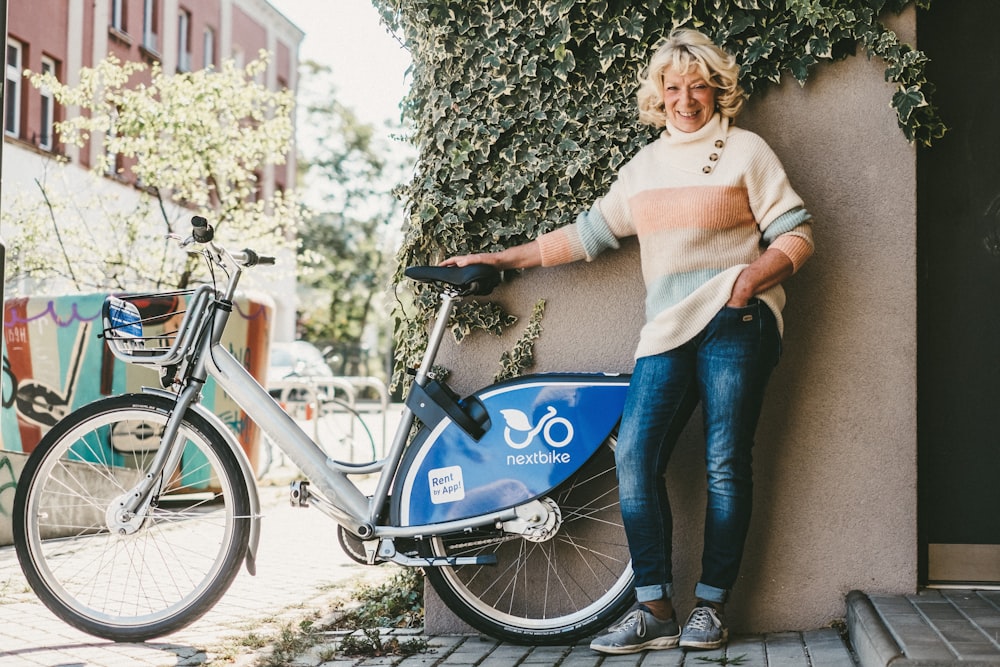woman in white long sleeve shirt and blue denim jeans standing beside blue bicycle during daytime