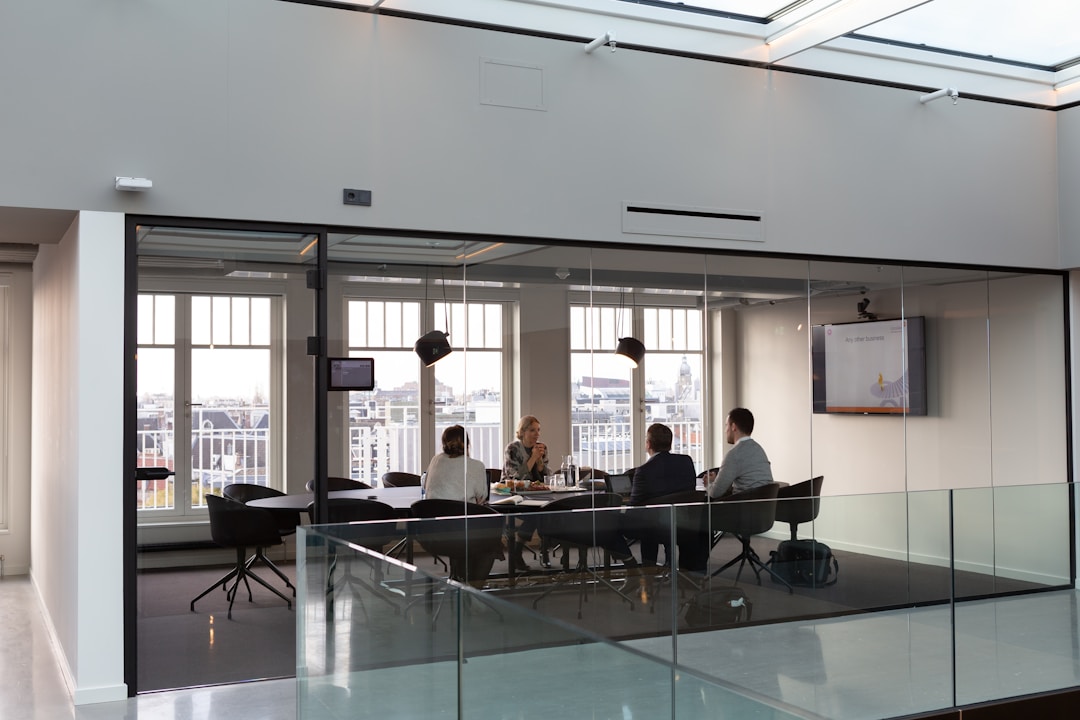 A proposal management meeting at a conference table in an all-glass windowed room.