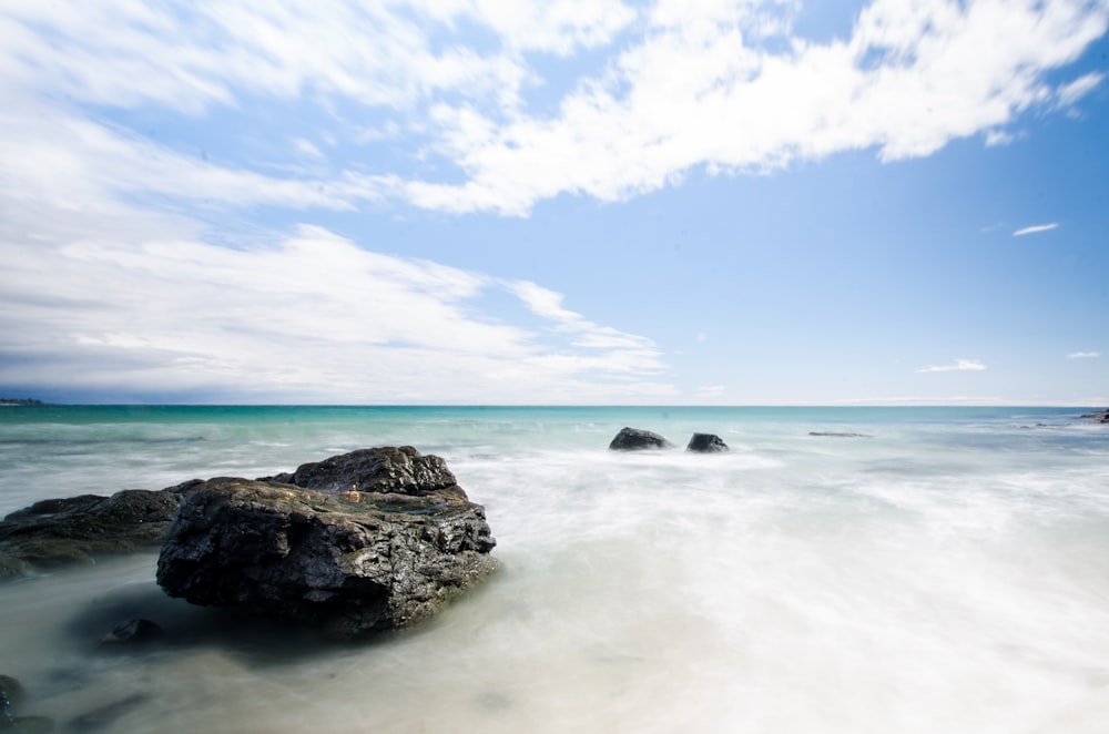 black rock formation on sea under blue sky during daytime