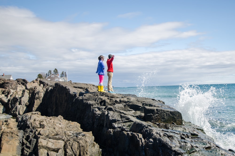 man in blue shirt standing on rock formation near ocean during daytime