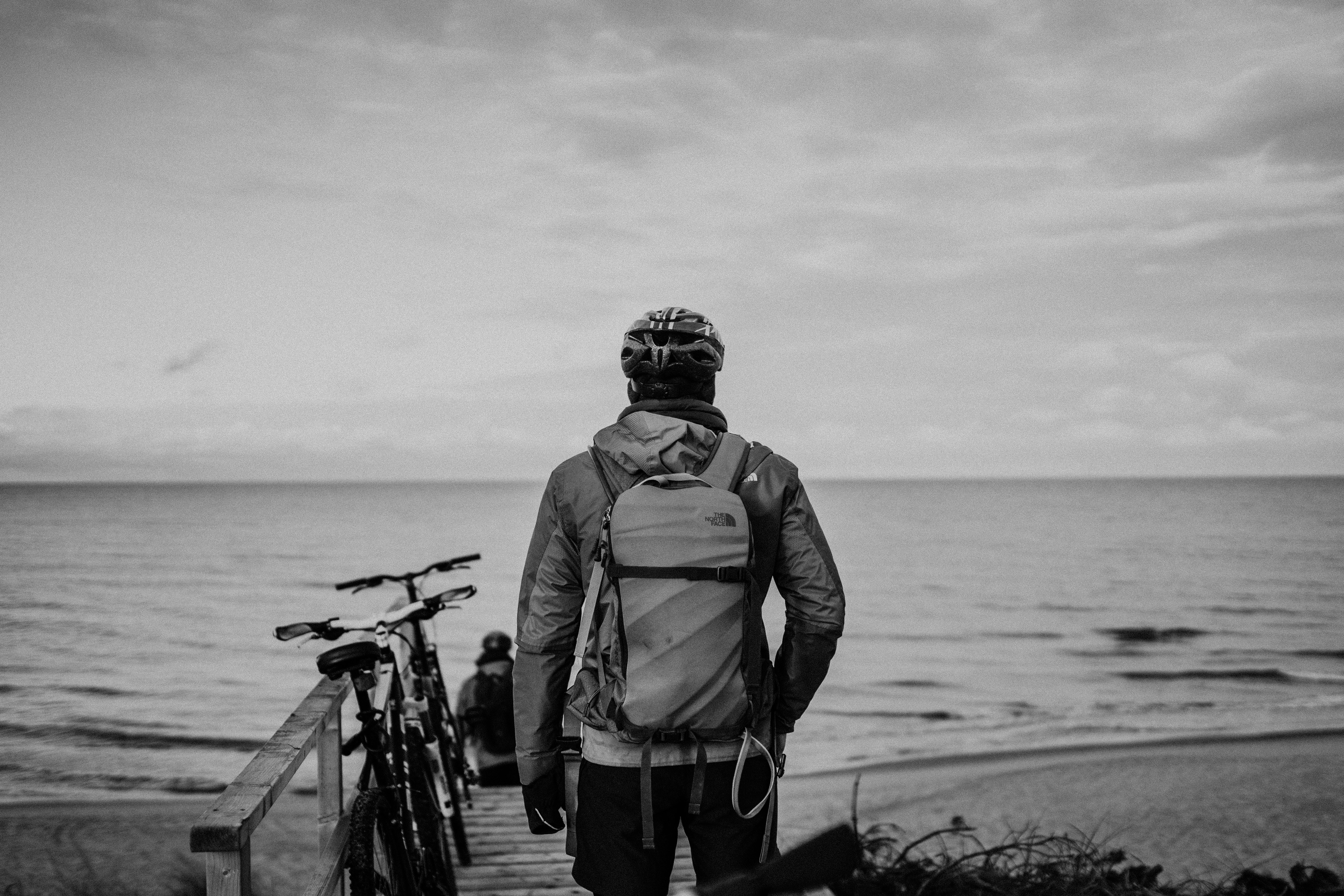 grayscale photo of man in jacket and helmet standing on beach