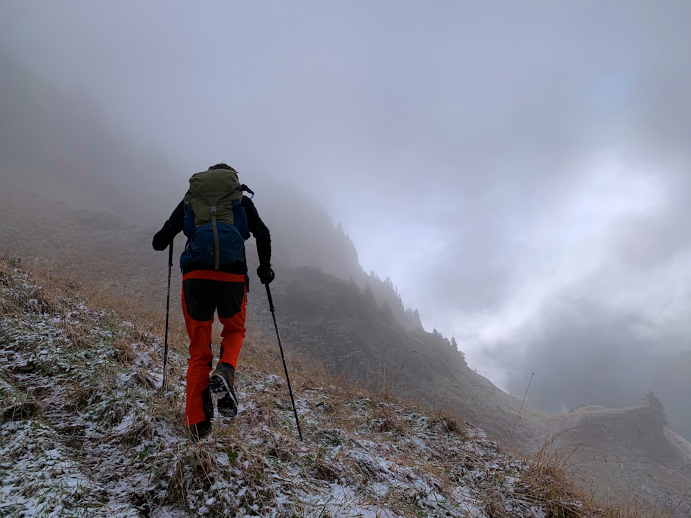 man in green jacket and red backpack walking on rocky road