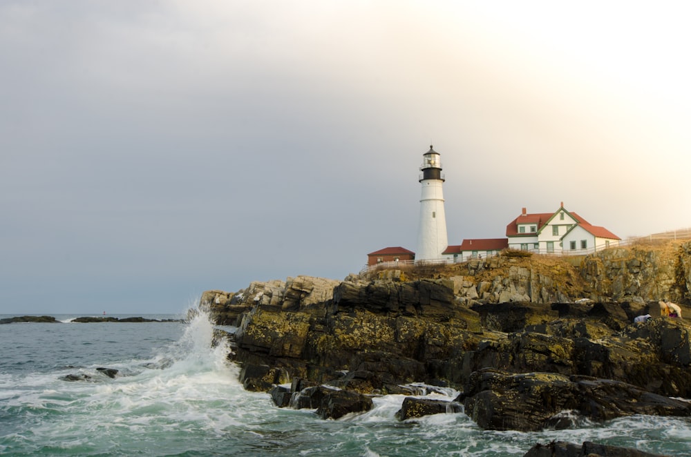 white and brown lighthouse on brown rock formation near body of water during daytime