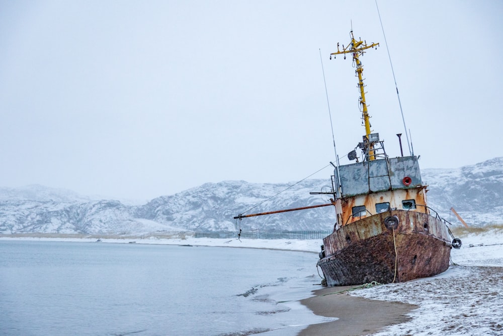 brown ship on sea near snow covered mountain during daytime