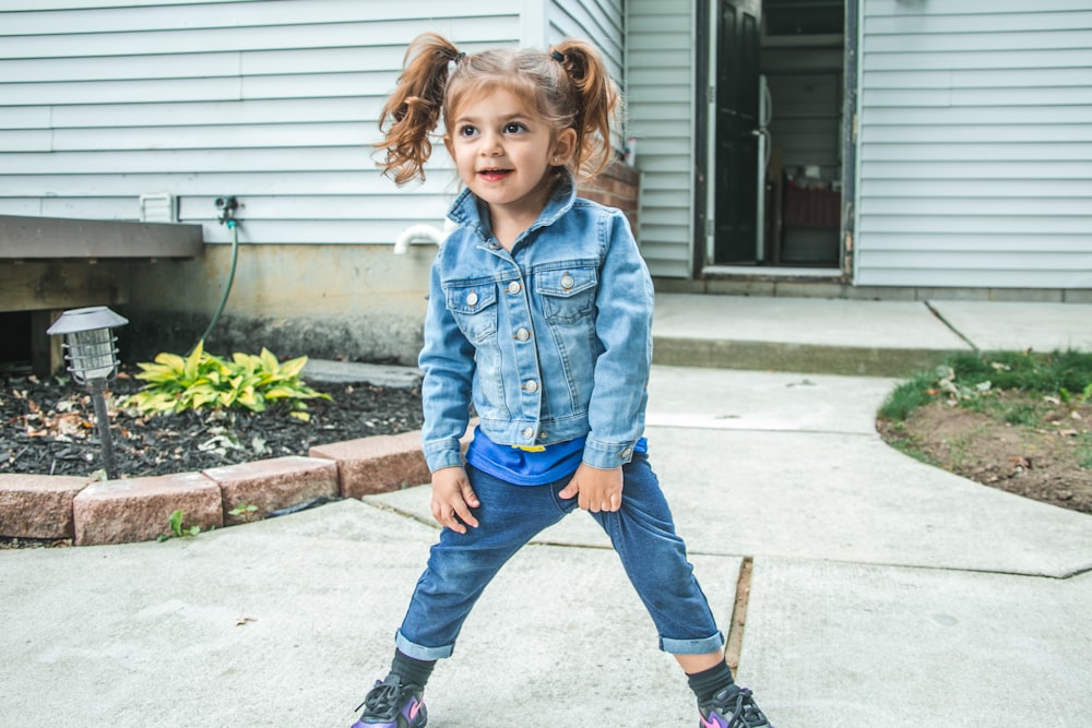 girl in blue denim jacket and blue denim jeans standing on gray concrete floor during daytime