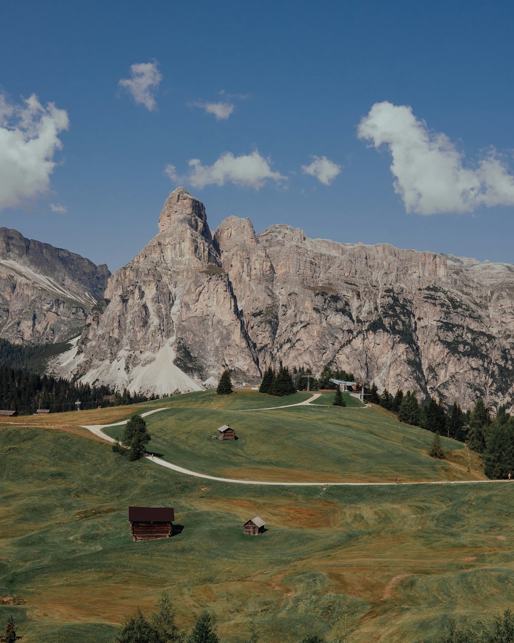 green grass field near gray rocky mountain under blue and white sunny cloudy sky during daytime