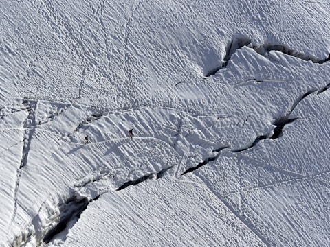 Close-up of travelers hiking across a shimmering blue glacier under clear skies.