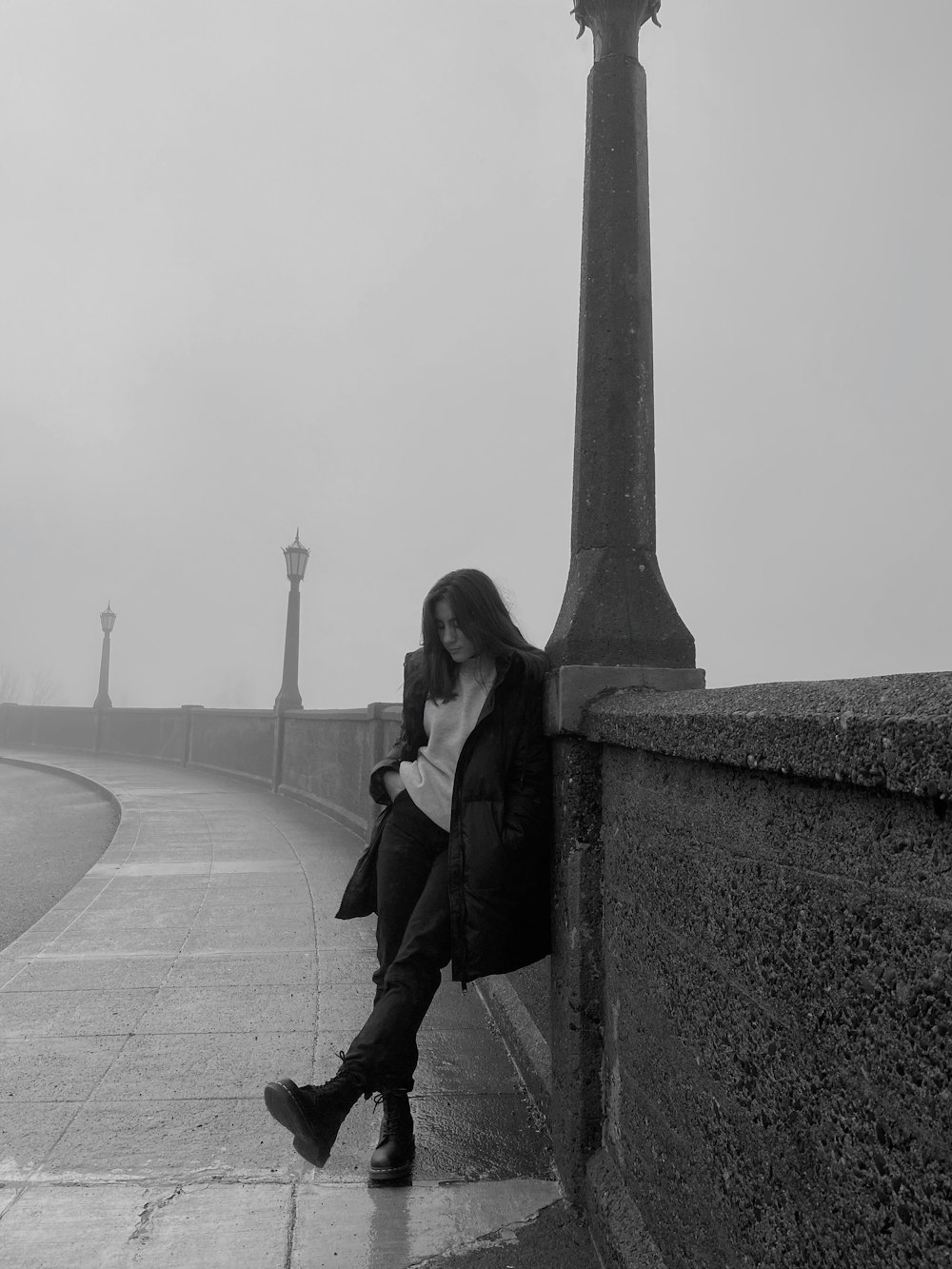 a woman sitting on a wall next to a lamp post