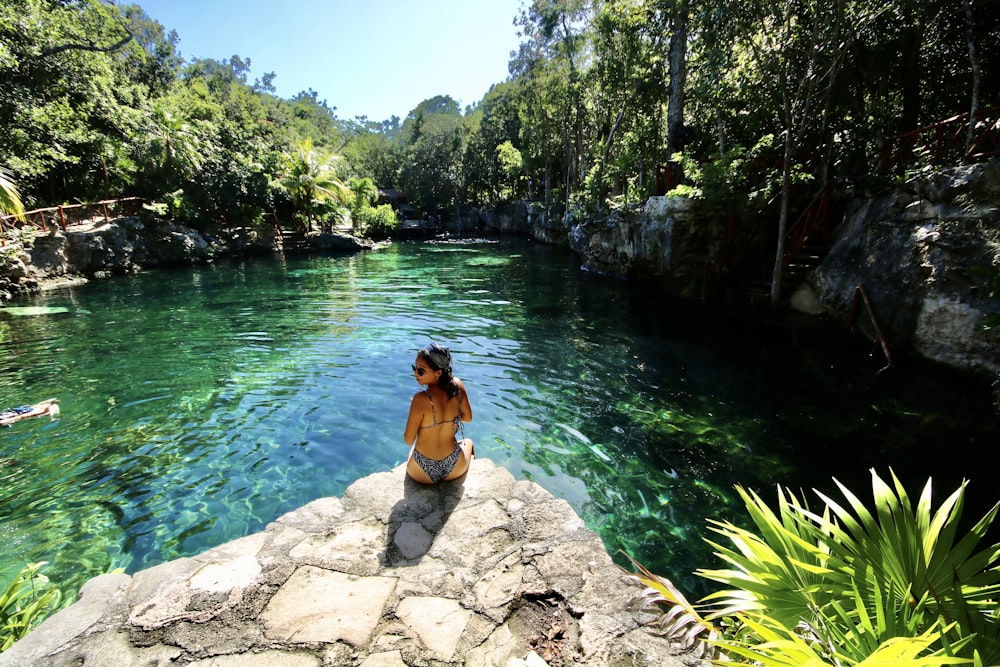 woman in black bikini sitting on rock near body of water during daytime